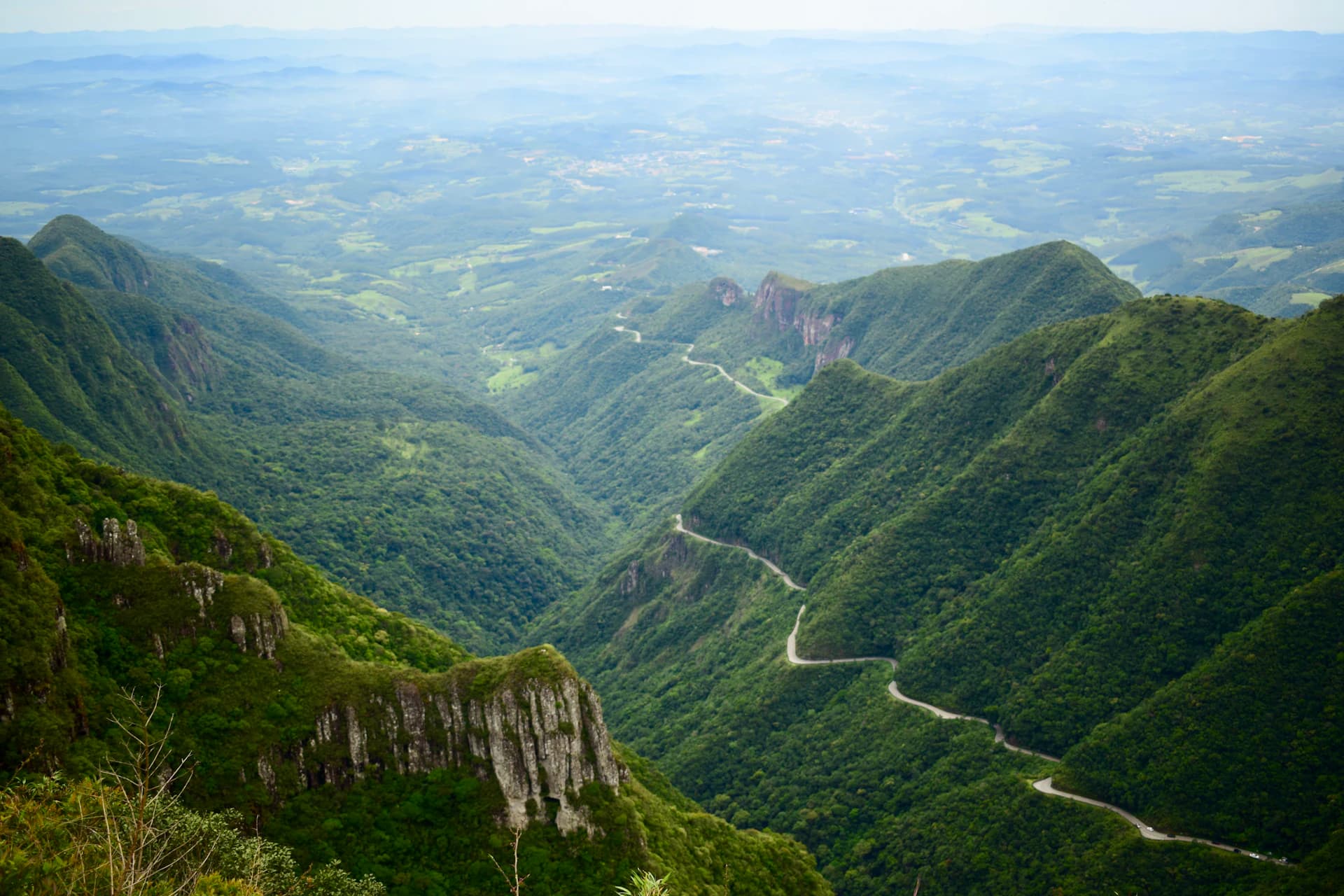Estrada sinuosa atravessando uma serra coberta de mata verde