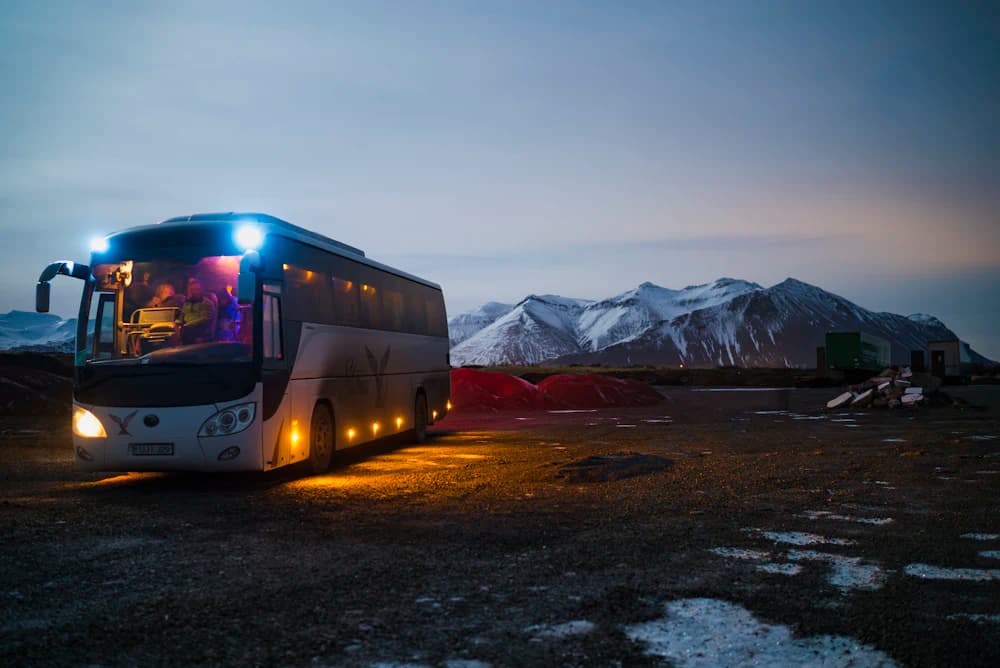 Ônibus de turismo com faróis acesos em uma estrada de montanha ao entardecer